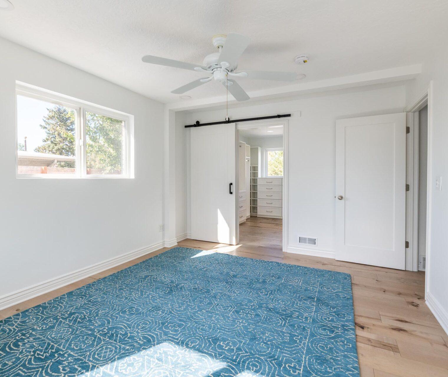 A room with a blue rug and a ceiling fan