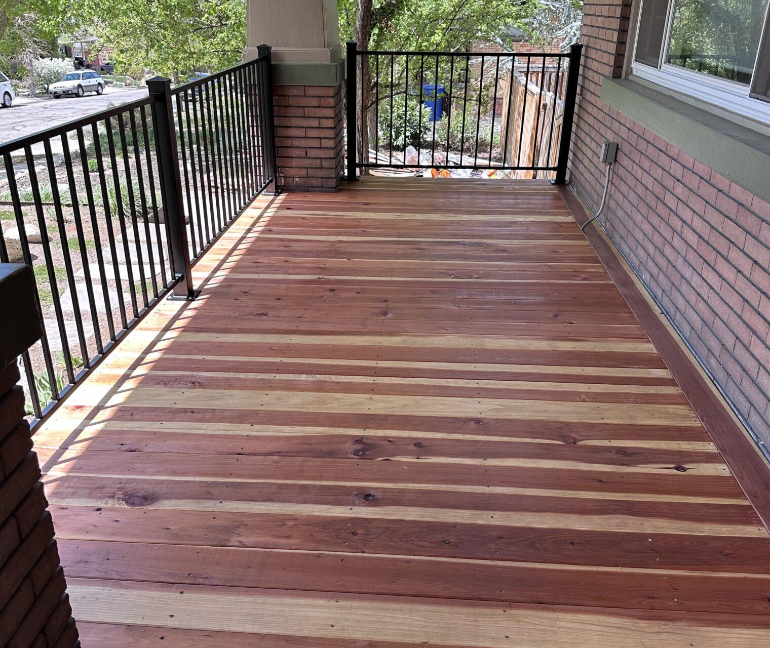 A wooden porch with a black railing and a brick wall