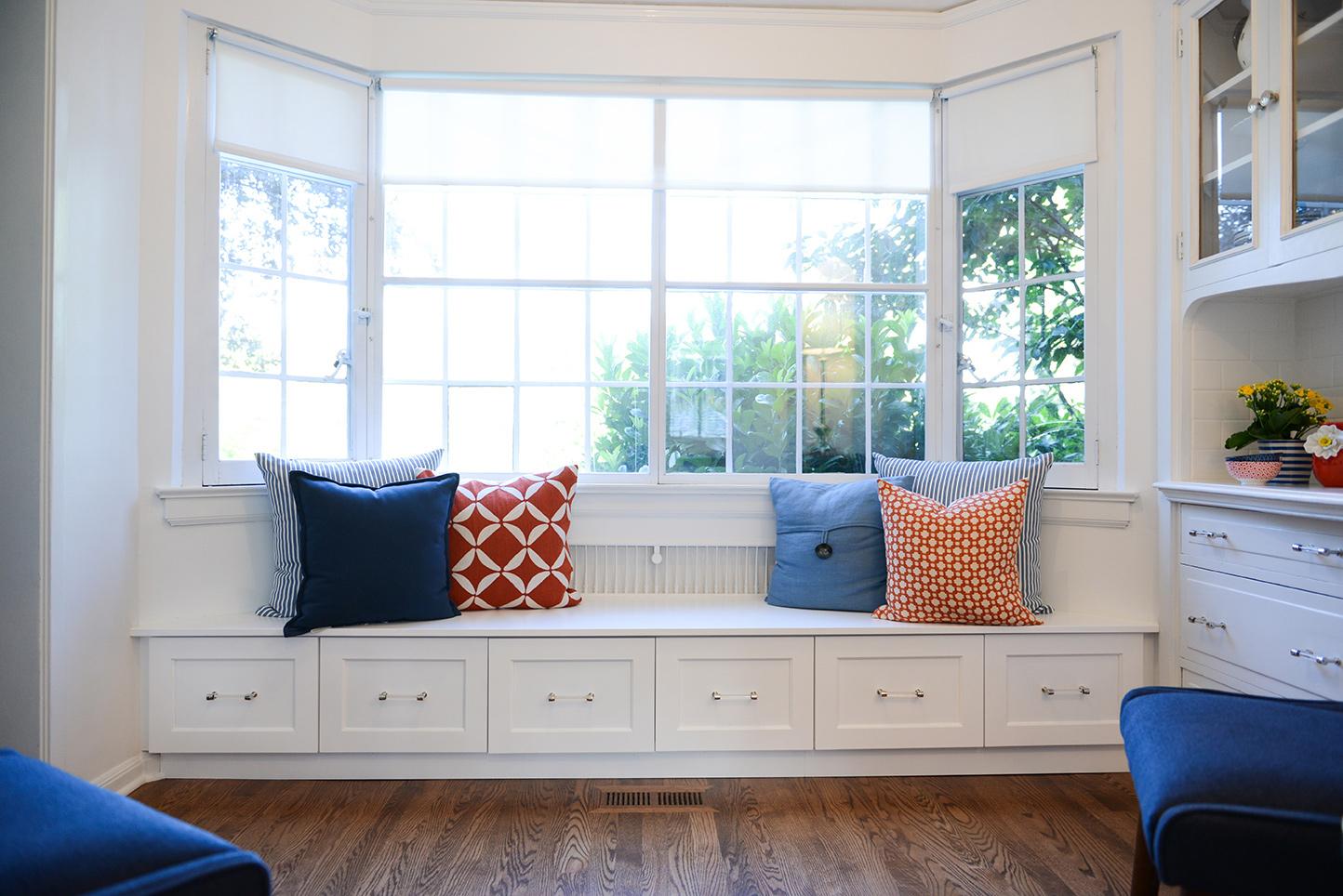 A white window seat with blue and orange pillows