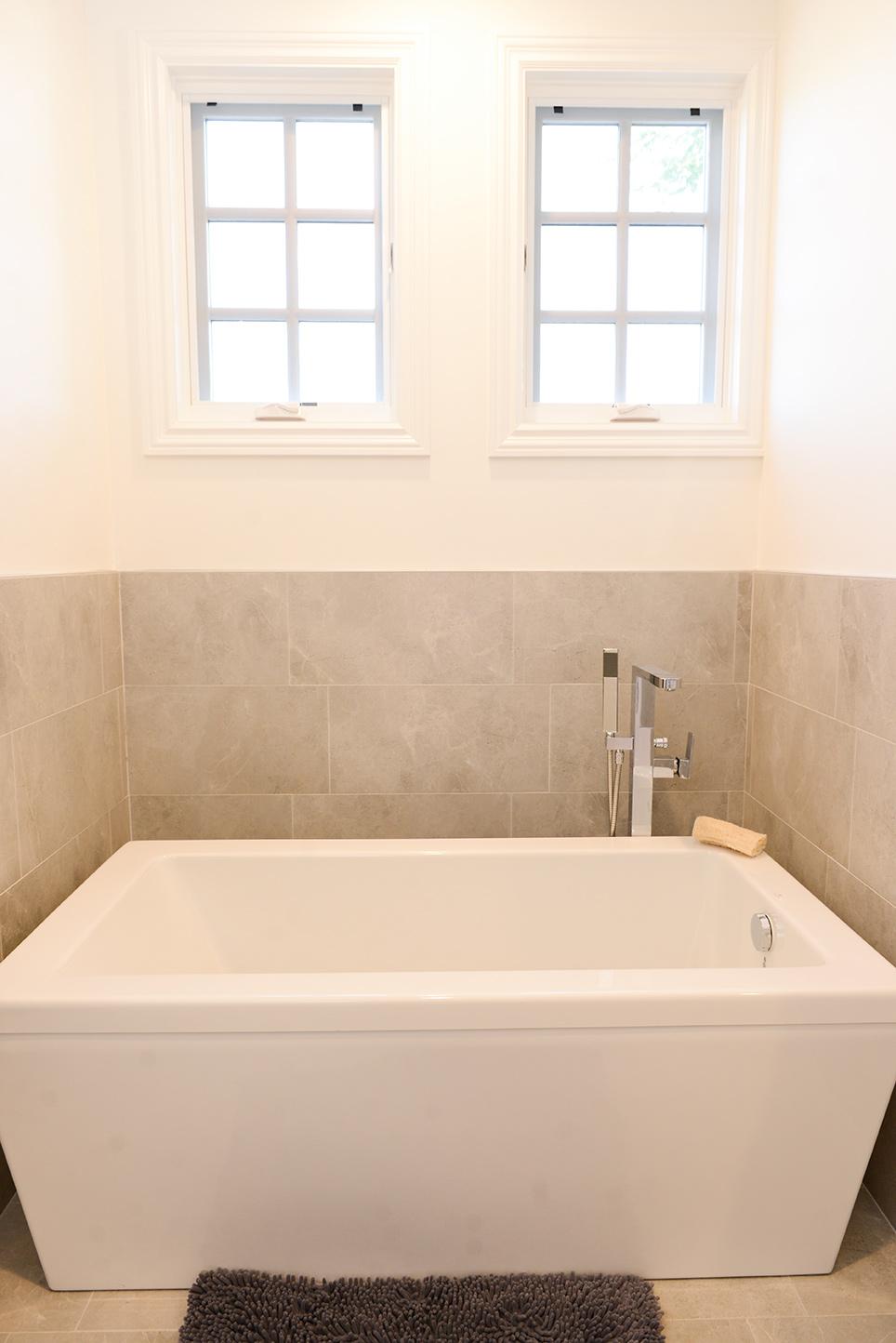 A white bath tub sitting under two windows