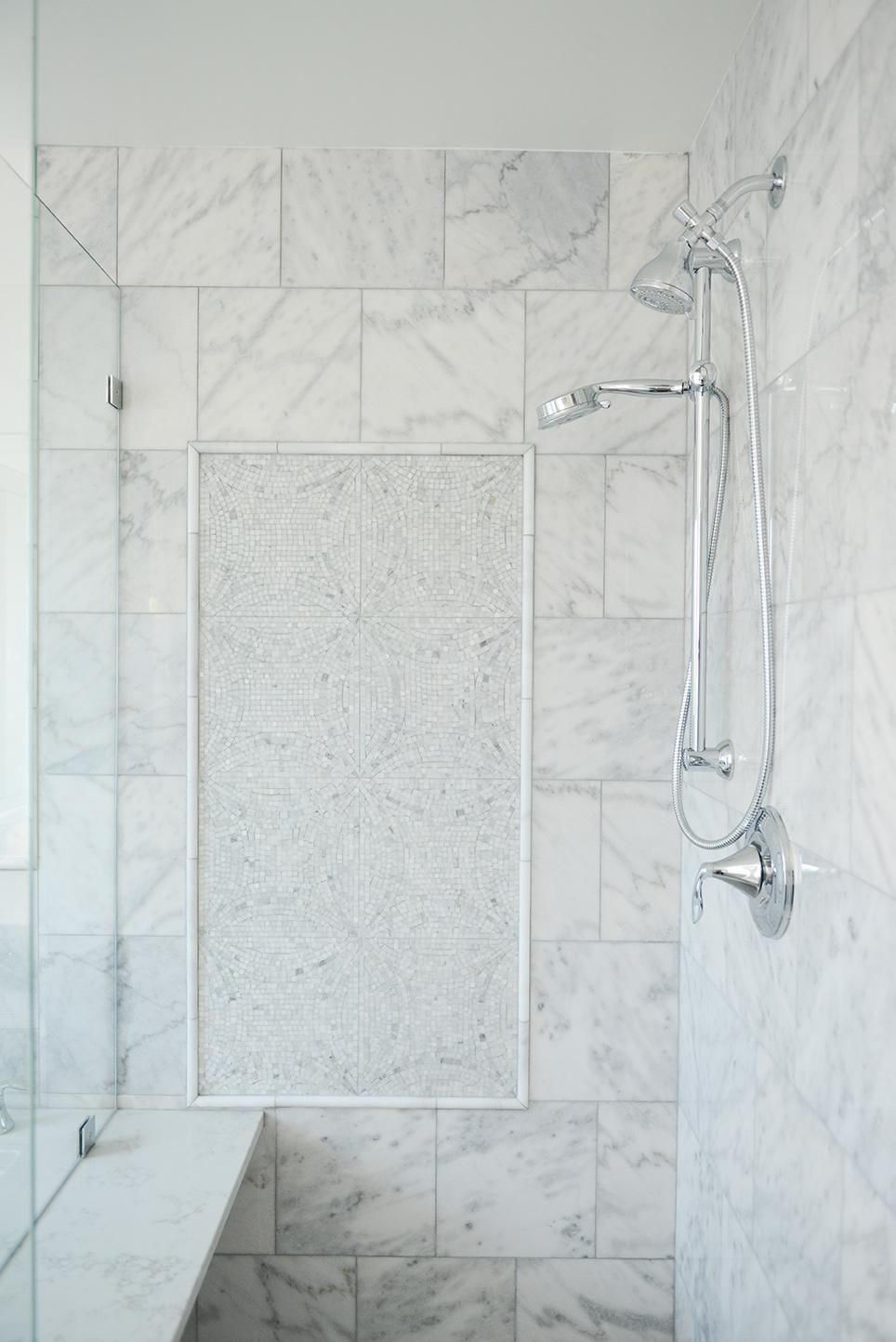 A bathroom with a white marble shower and a white bench