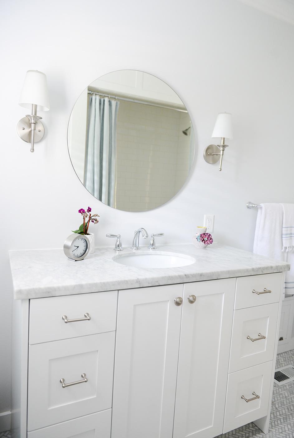 A white bathroom with a large round mirror