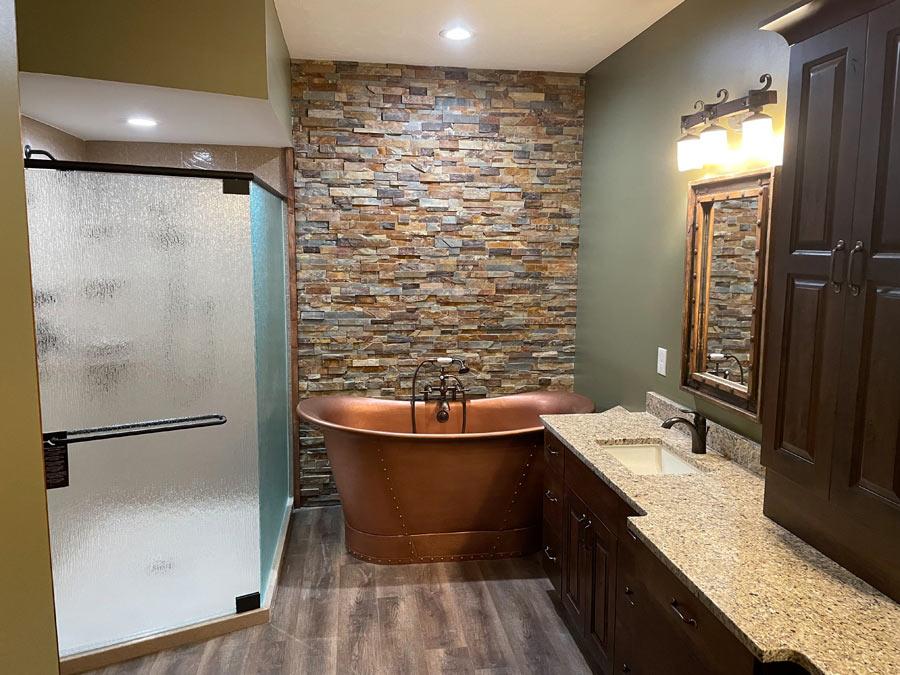 A bathroom with a stone wall and a copper bathtub